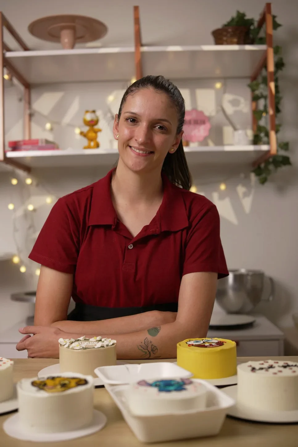 Amanda Vicente sorrindo na confeitaria, cercada por bentô cakes que ensina a decorar