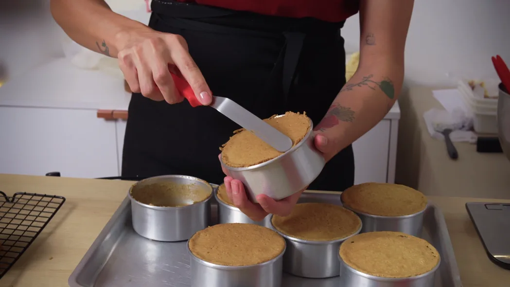 Cena da aula de massas: a Amanda nivela a massa de bolo assada em uma pequena forma